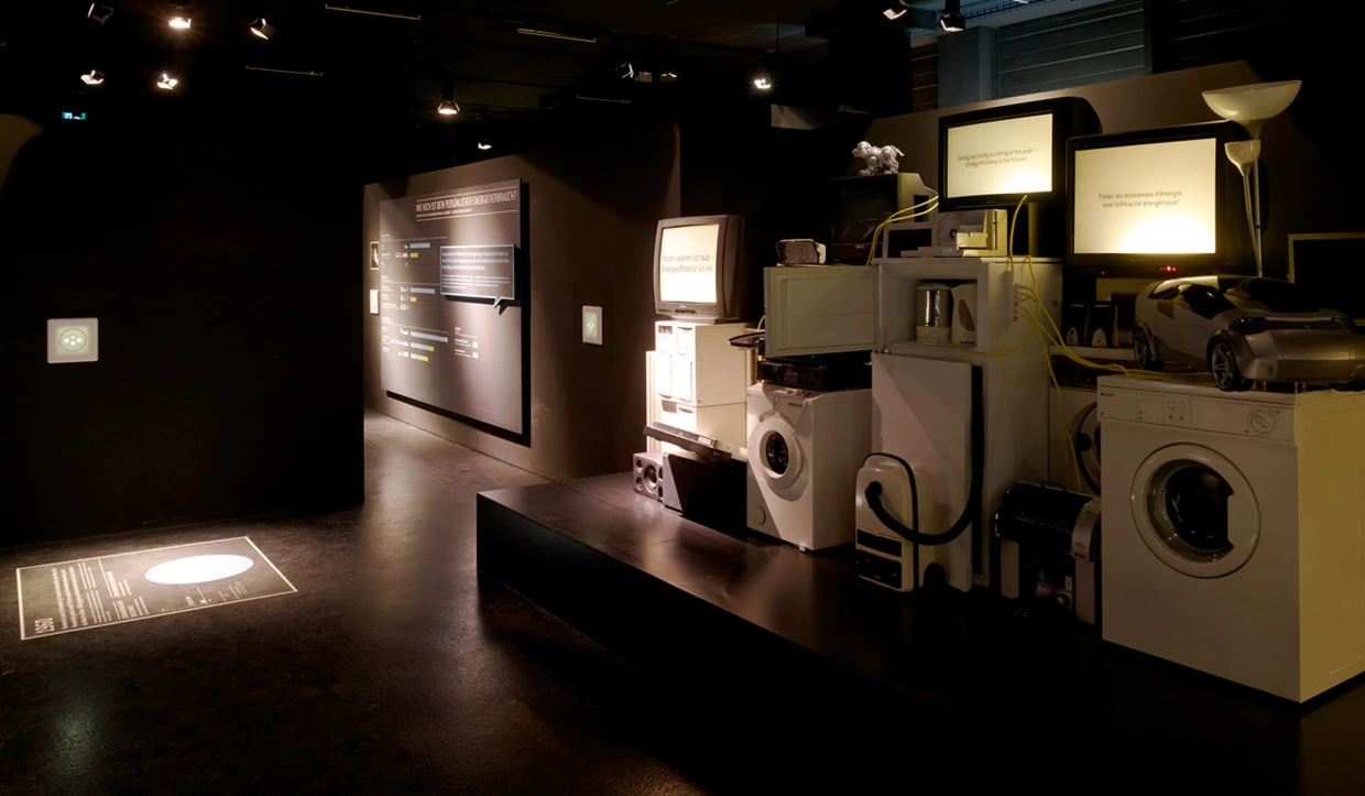 Dunkler Ausstellungsraum mit Energiespargeräten und Infotafeln