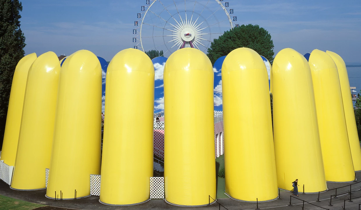 Gelbe aufblasbare Strukturen vor einem Riesenrad und Wolkenbildern