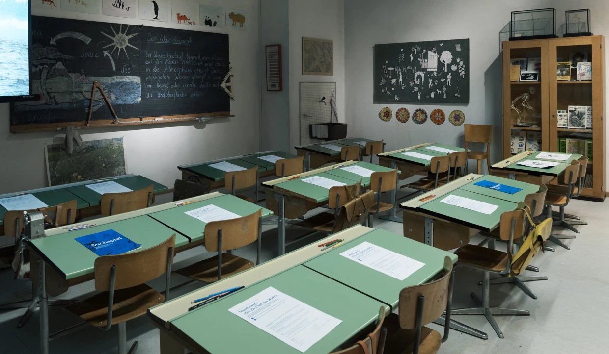Klassenzimmer mit grünen Tischen und Tafeln an den Wänden