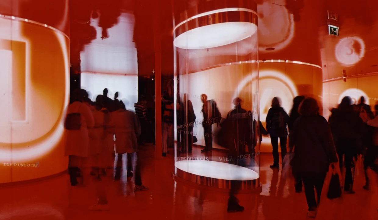 People in a room with red lighting and reflective surfaces