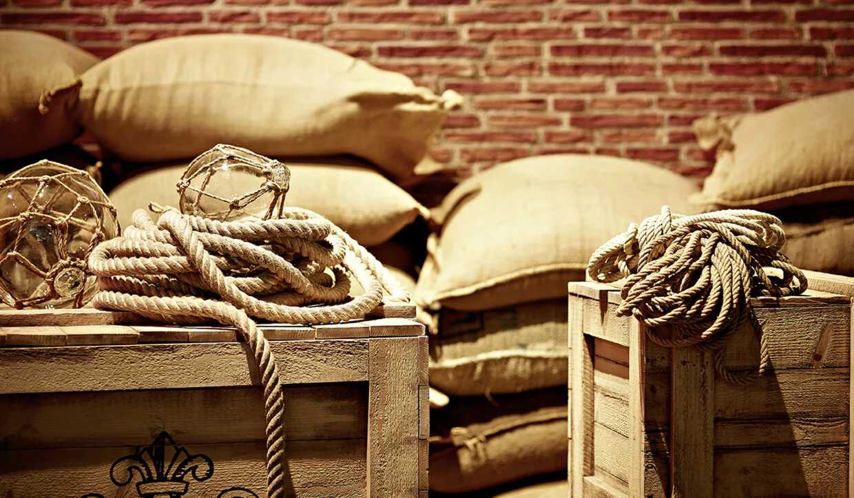 Seile und Holzkisten vor Kaffeesäcken mit Ziegelwandhintergrund