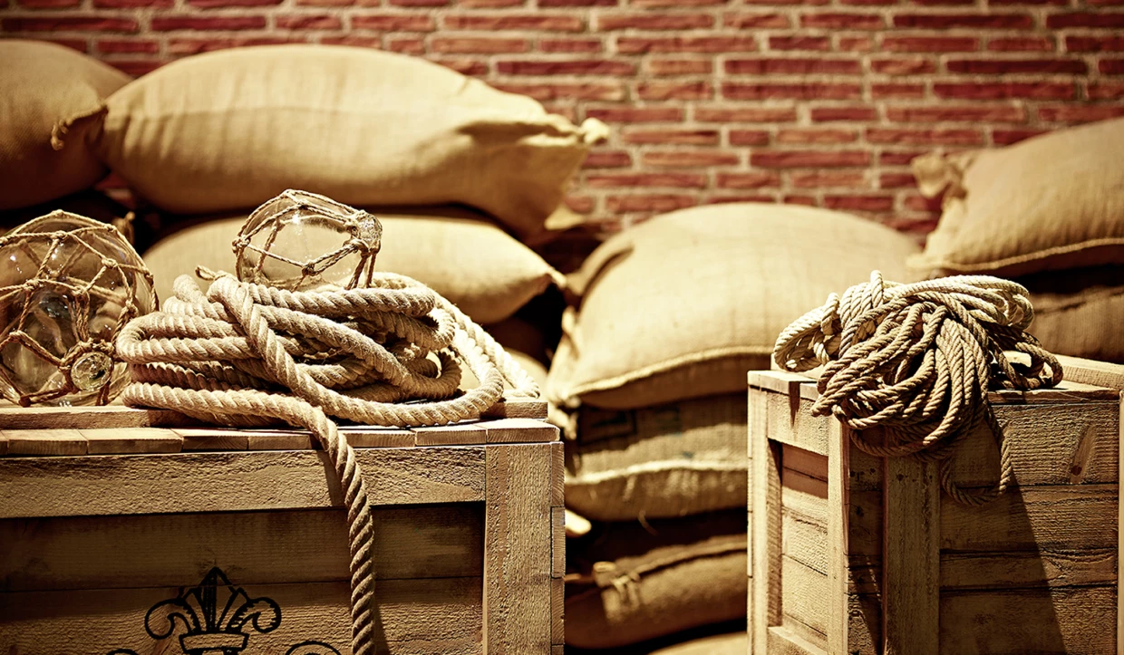 Ropes and wooden crates in front of coffee sacks with brick wall background