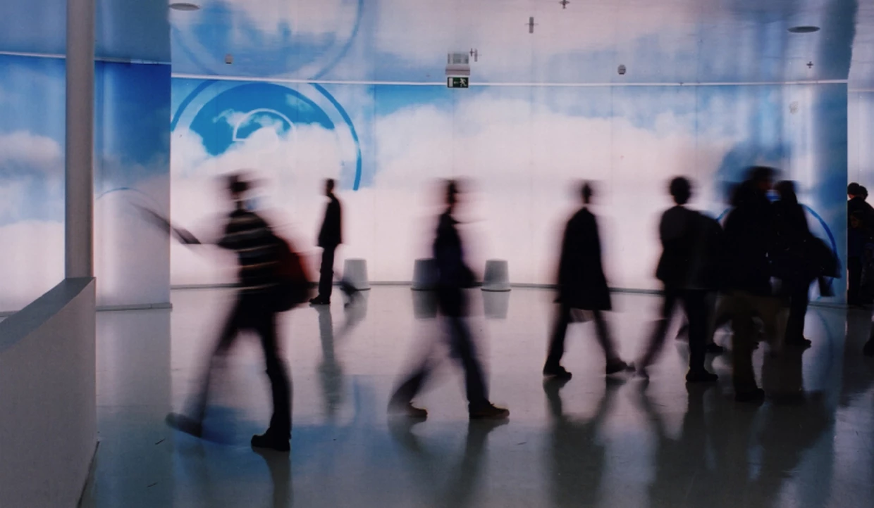 Blurred people walking past a blue wall with cloud motif