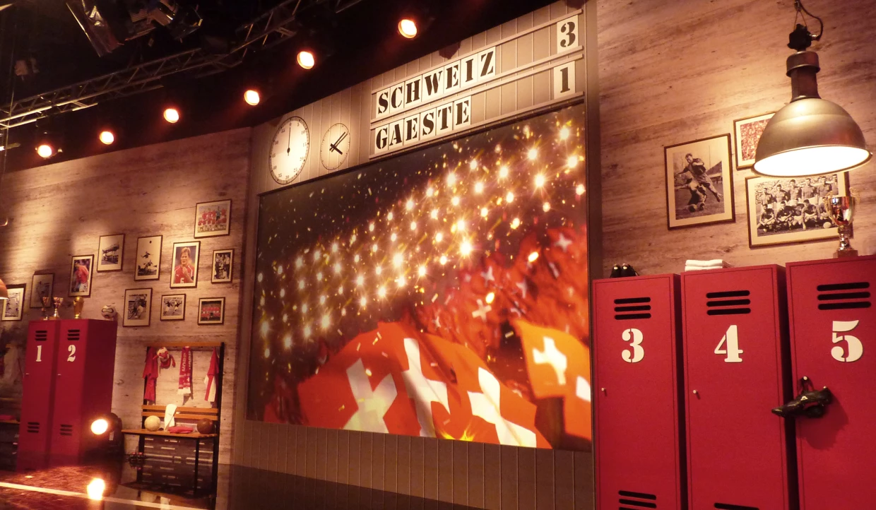 Anzeigetafel mit Spielstand Schweiz 3, Gäste 1, rote Spinde und Fotos