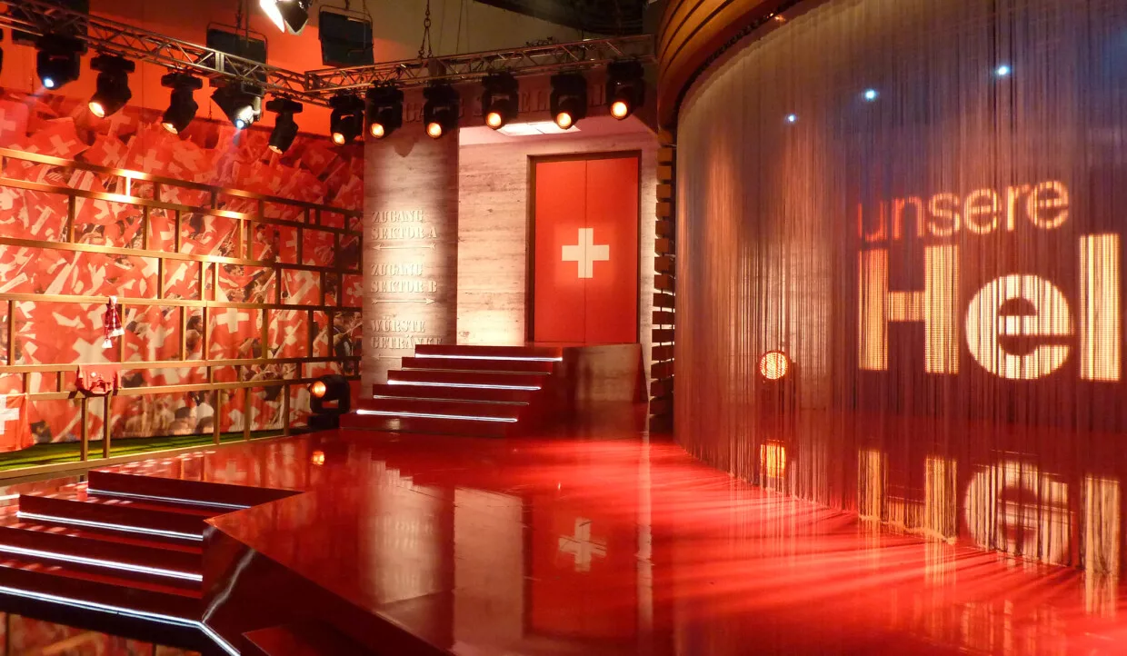 Stage design with red lighting, Swiss flags, and 'unsere Helden' text