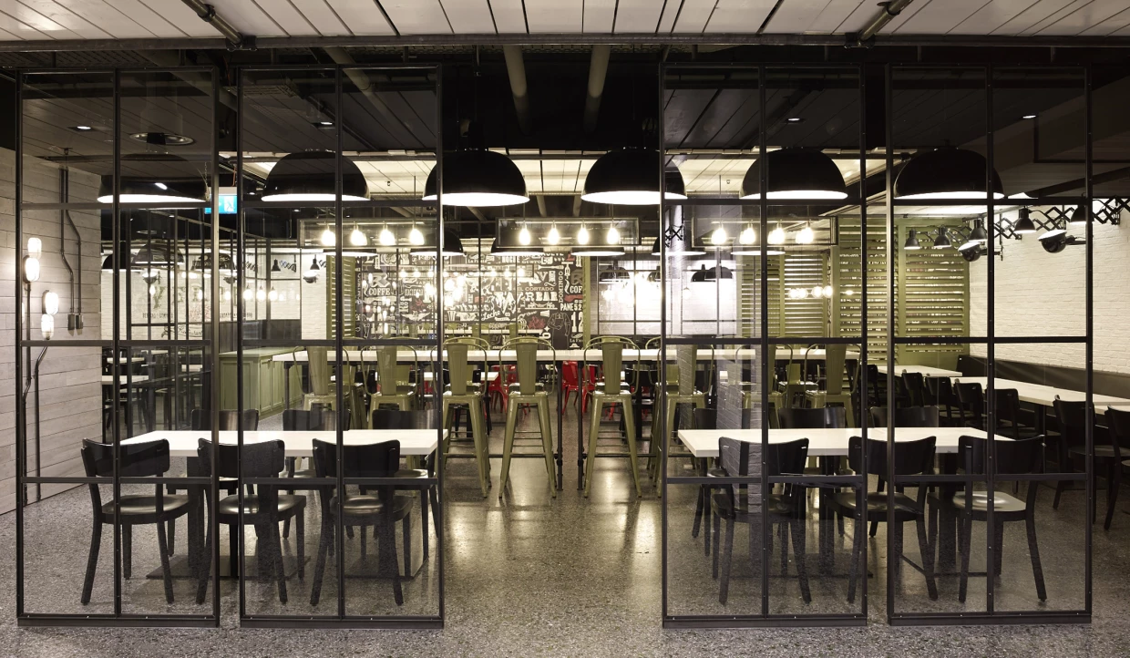 Glass panels divide restaurant areas with tables and lamps.