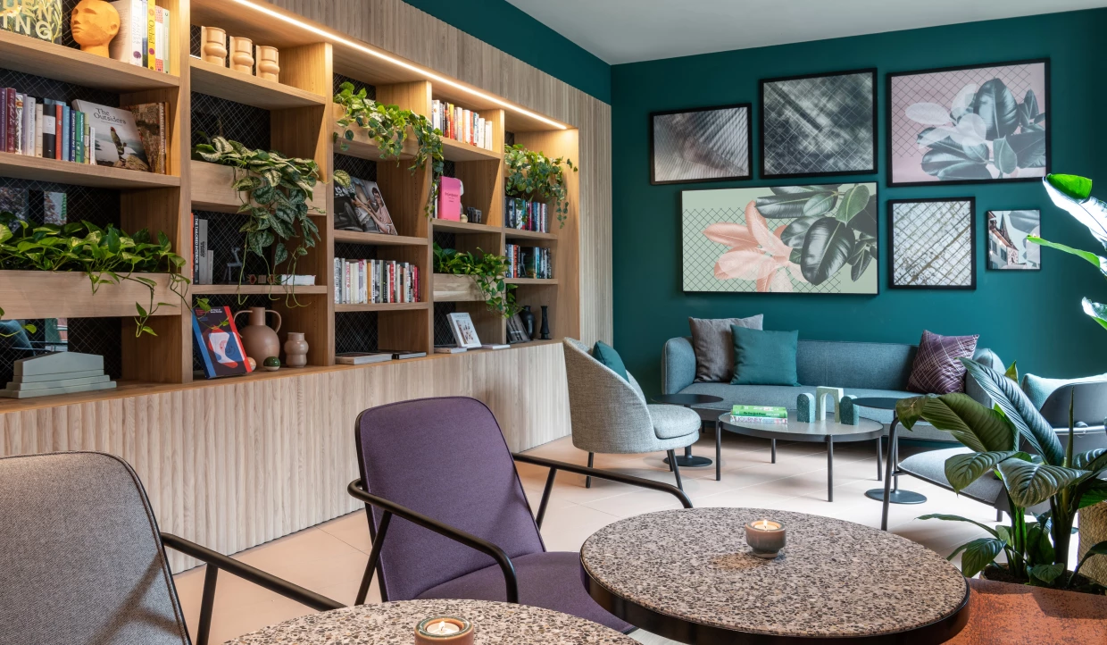 Lobby mit Bücherregalen voller Pflanzen, Pflanzengrafiken an der Wand und modernen Loungemöbeln in Türkis, Lila und Grau.
