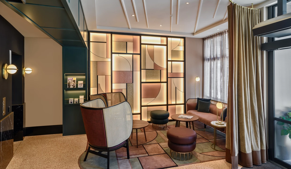 Hotel-Lobby mit moderner Leuchtwand mit Art-Deco-Motiven. Im Vordergrund Lounge-Möbel mit Wiener Geflecht.