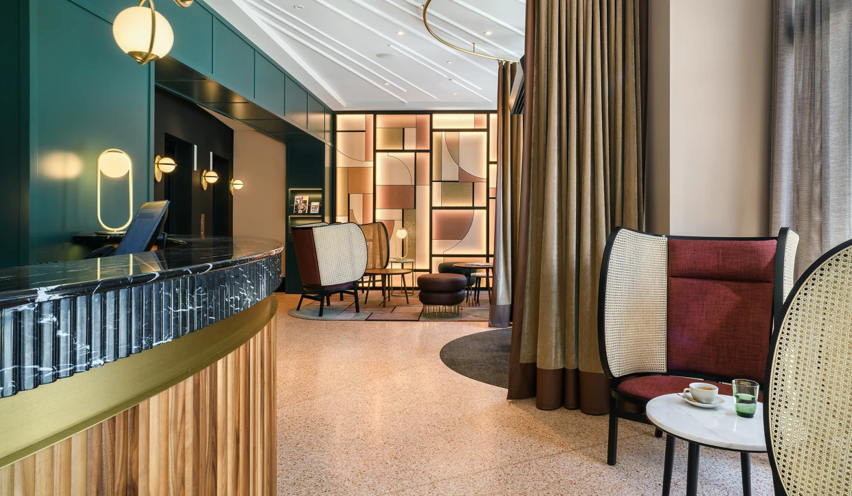 Hotel-Lobby mit Reception, moderner Leuchtwand im Art-Deco-Stil und Sesseln mit Wiener Geflecht.
