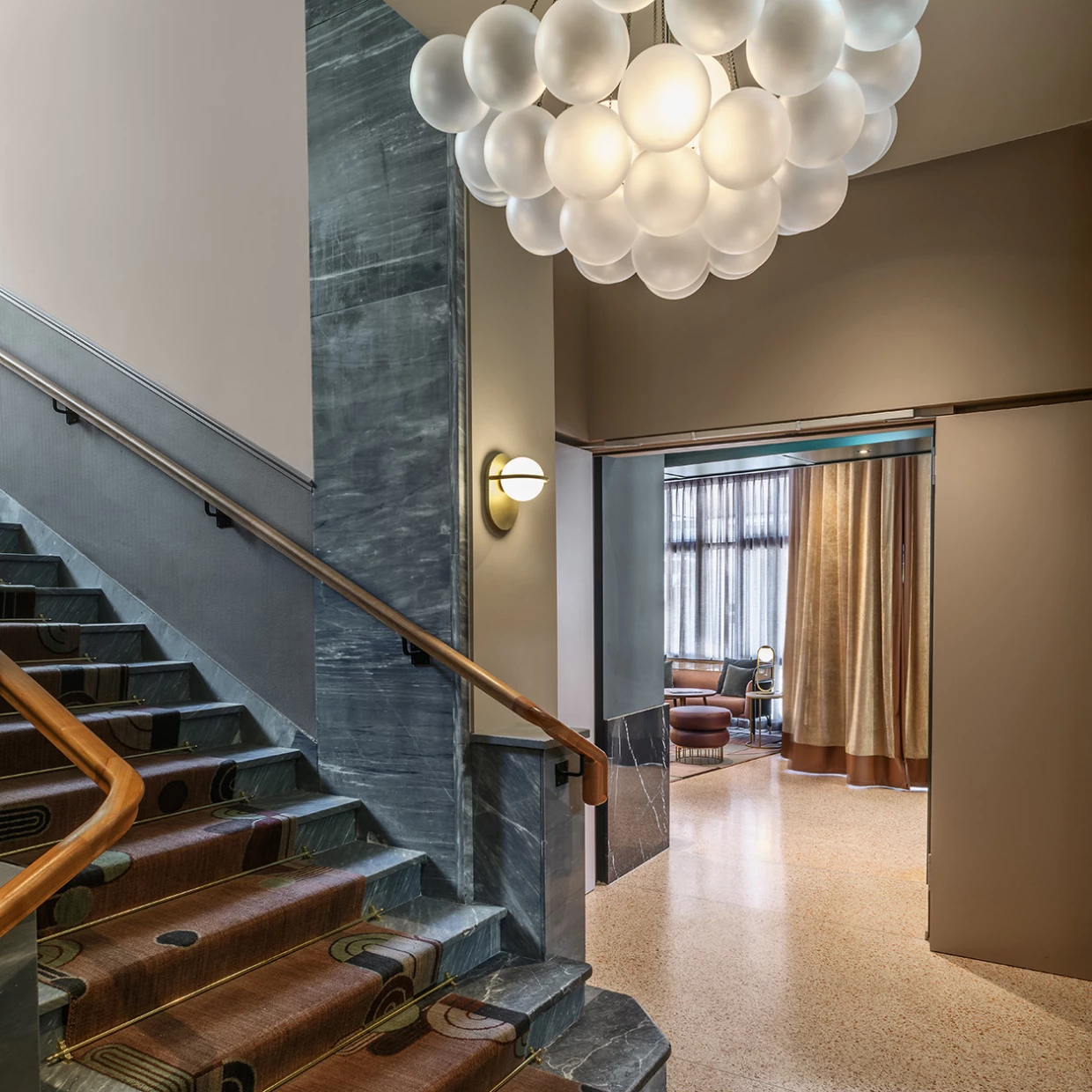 Treppe mit Teppich, großer Kugelleuchte und Blick in Richtung Hotel-Lobby mit Loungemöbeln.