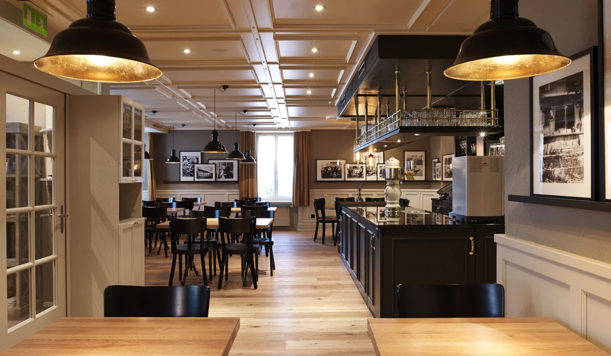 Innenansicht eines Restaurants mit dunkler Bar, Holztischen und gerahmten Fotos an den Wänden.