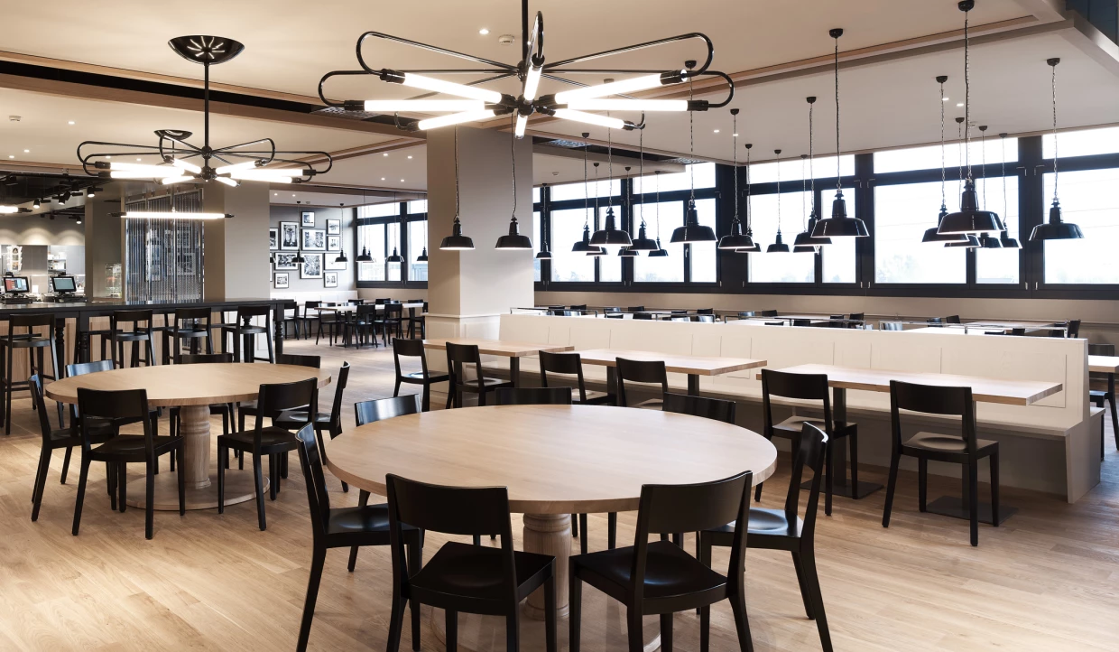 Modernes Restaurant mit runden Holztischen und schwarzen Stühlen.