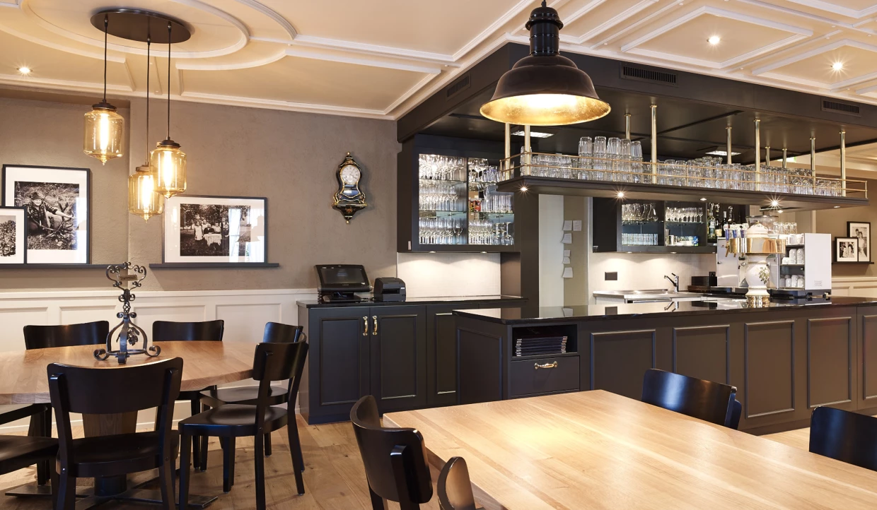 Modernes Restaurant mit schwarzen Stühlen, Holztheke und Glasregalen hinter der Bar.
