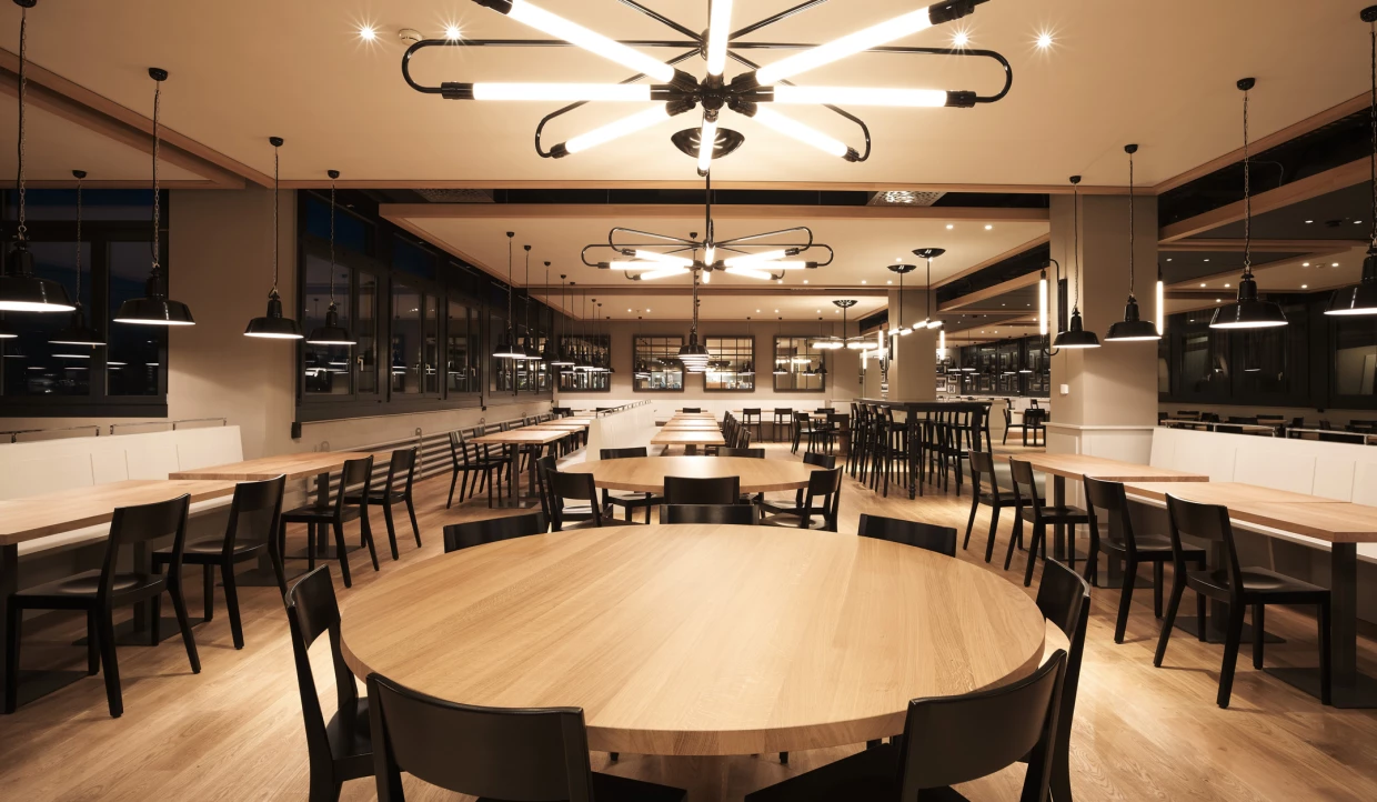 Restaurant bei Nacht mit beleuchteten runden Tischen und Lampen.