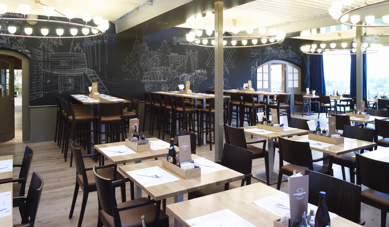 Restaurant mit Tischen, Stühlen und schwarzen Wandzeichnungen.