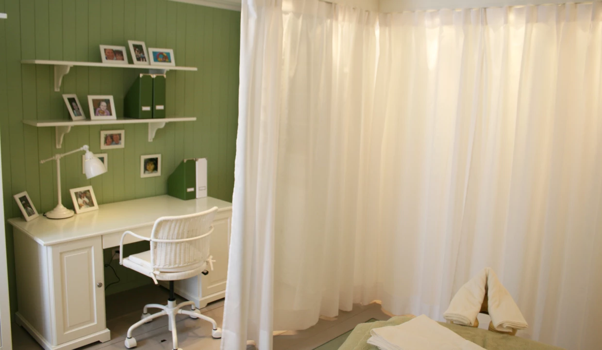 Arbeitszimmer mit grünem Regal, Schreibtisch und Vorhängen
