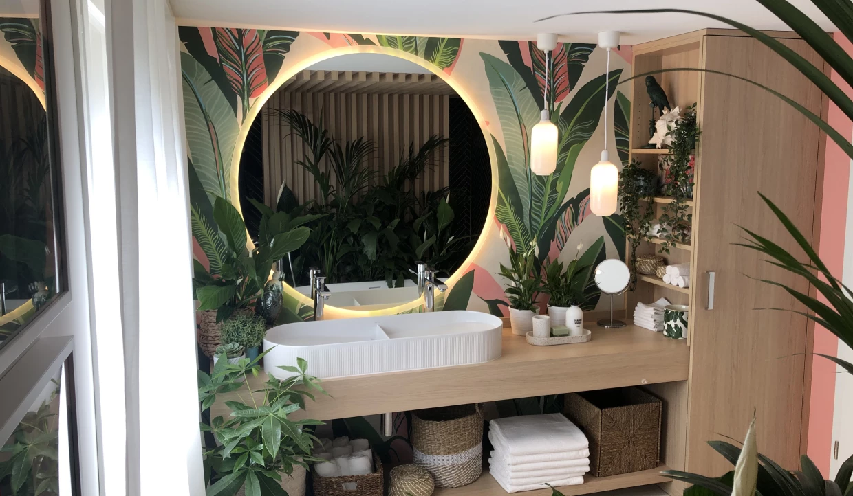 Badezimmer mit Pflanzen, beleuchteter Rundspiegel und Holzregal