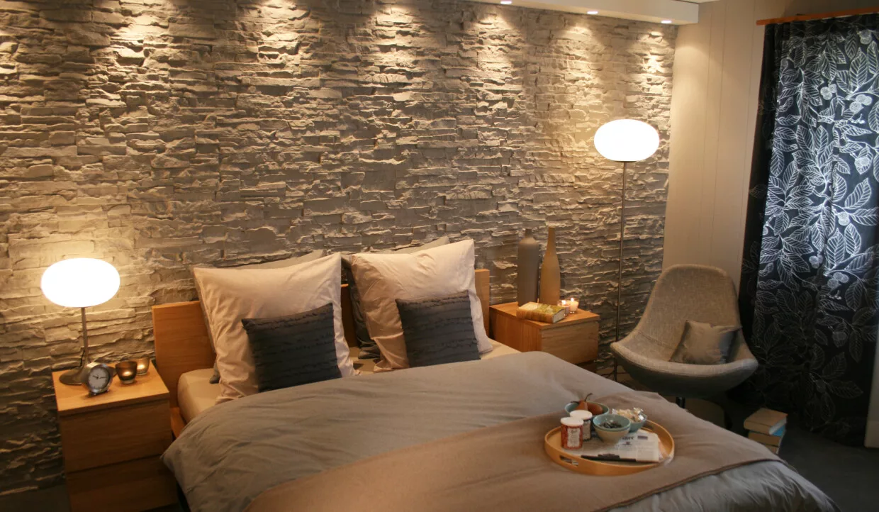 Doppelbett vor Steinwand mit Stehlampen