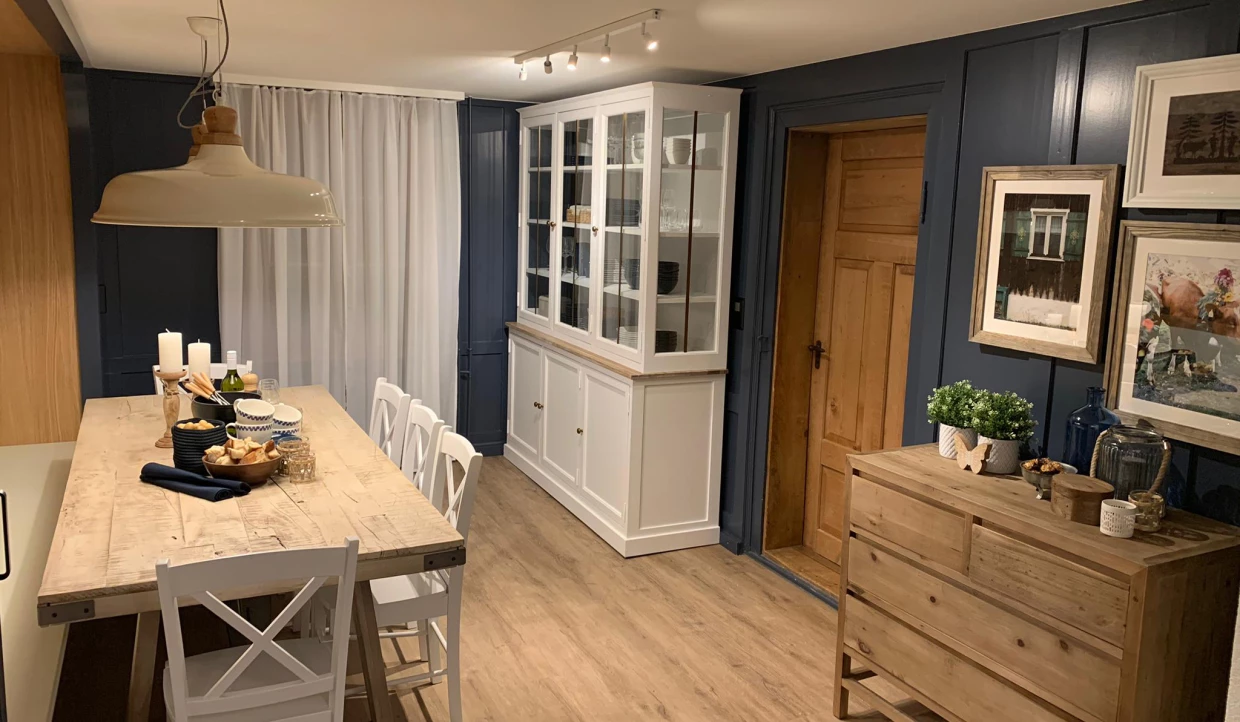 Esszimmer mit Holztisch, weißen Stühlen, Vitrine und Dekoration