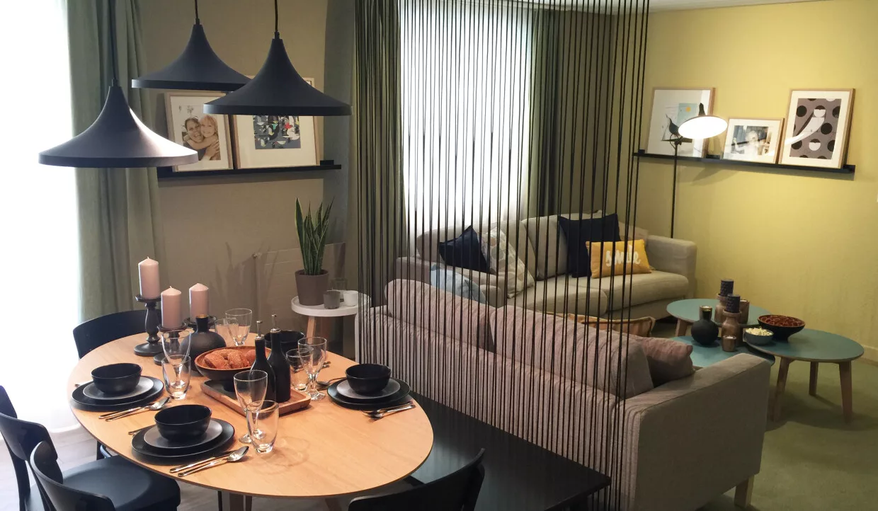 Esszimmer mit Holztisch, schwarzen Tellern und Hängelampen, Wohnzimmer im Hintergrund