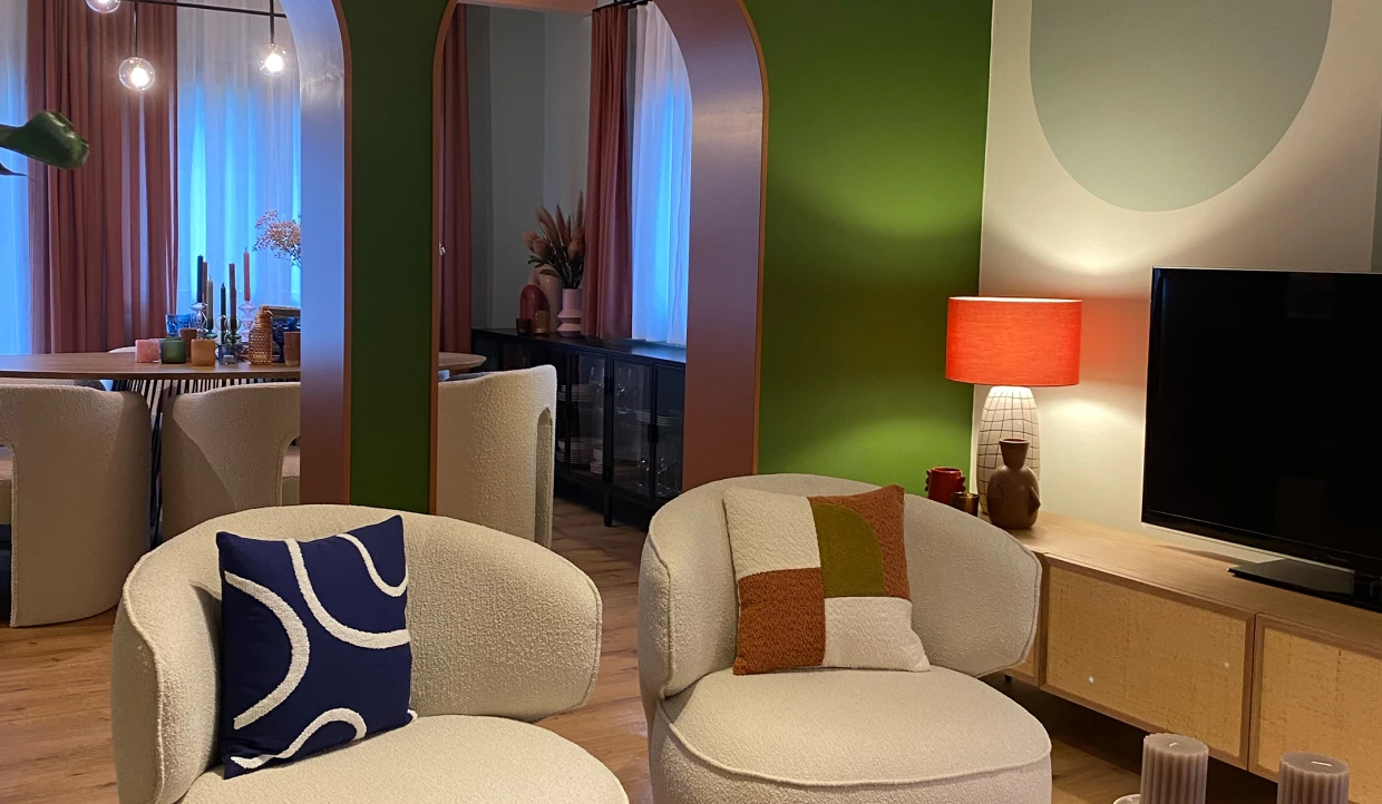 Modernes Wohnzimmer mit cremefarbenen Sesseln und farbigen Kissen vor grünem Hintergrund
