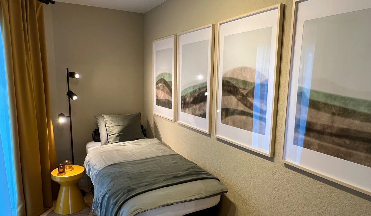 Schlafzimmer mit Einzelbett, gelber Vorhang und vier Bildern