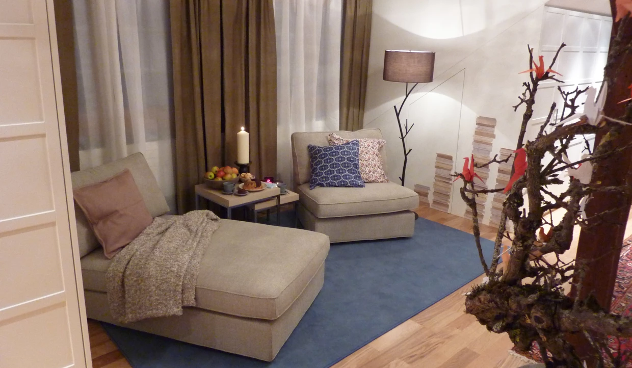 Sitzecke mit zwei hellgrauen Sesseln, blauem Teppich und Tisch mit Snacks