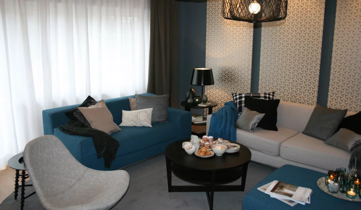 Wohnzimmer mit blauen Sofas, rundem Tisch und Lampe