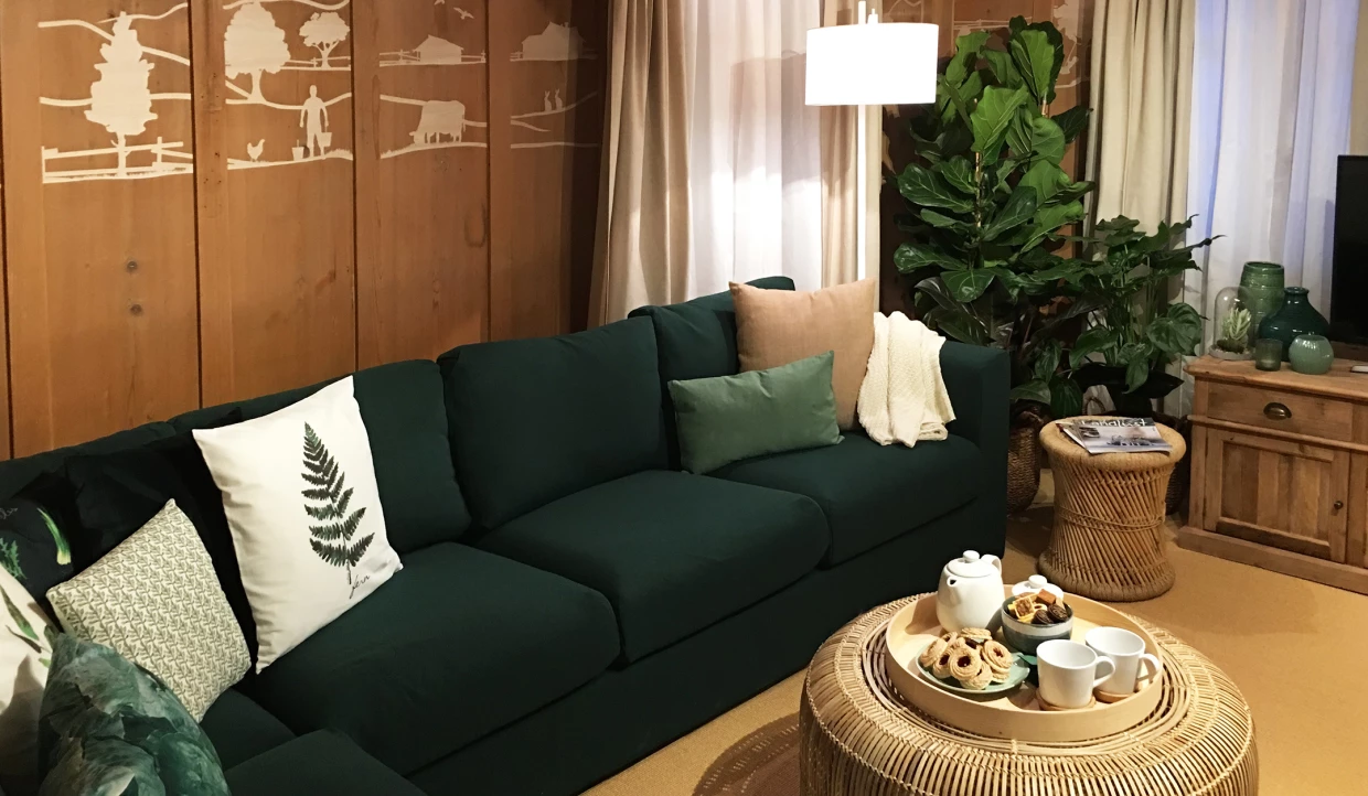 Wohnzimmer mit grüner Couch, Kissen, Pflanzen und Holzmöbeln