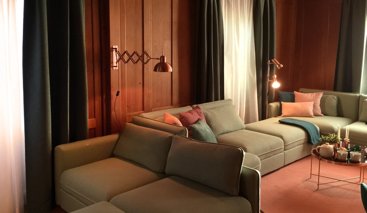Gemütliches Wohnzimmer mit grünem Sofa, Kissen und Vorhängen