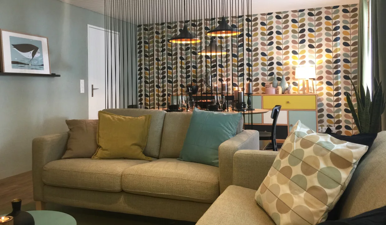 Wohnzimmer mit Sofa, bunten Kissen, Esszimmer mit runden Hängelampen