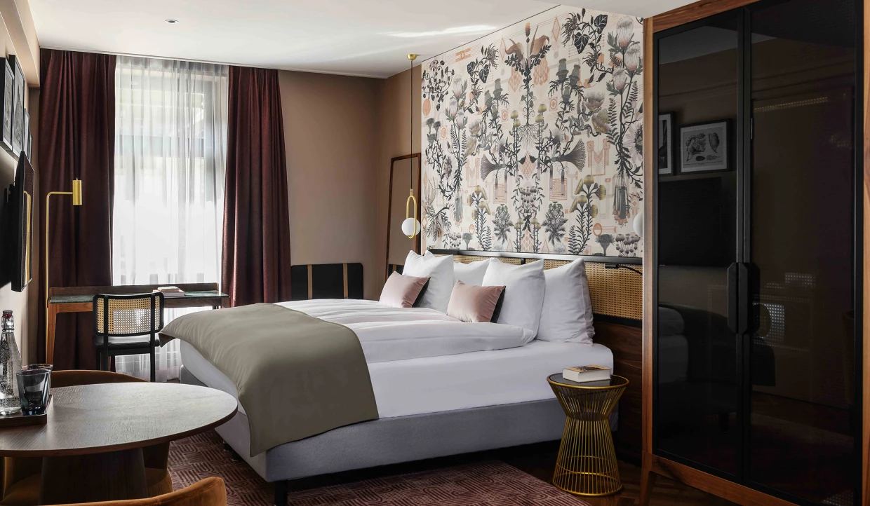 Historisch inspiriertes Hotelzimmer mit Doppelbett in warmen Farben. Individuelle Tapete im Art-Deco und Jugenstil-Mix.