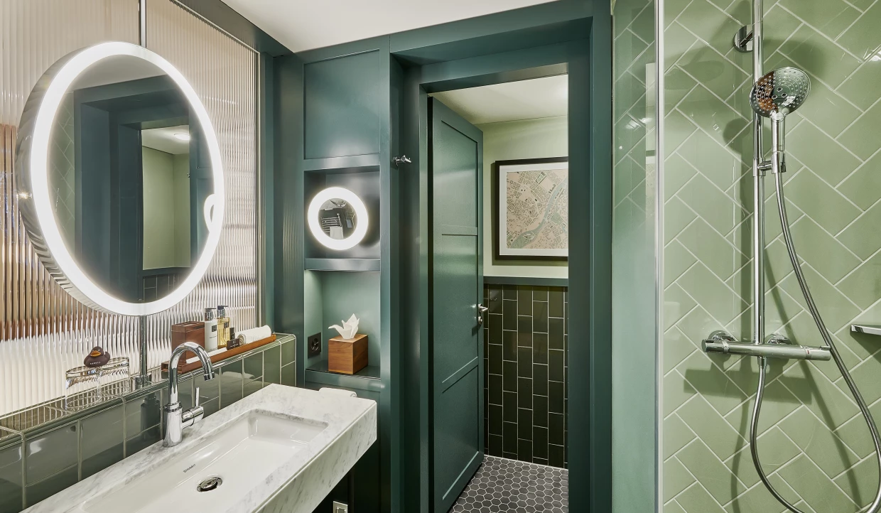 Elegantes Badezimmer in Grüntönen mit historischen Elementen, beleuchtetem Spiegel und Dusche.
