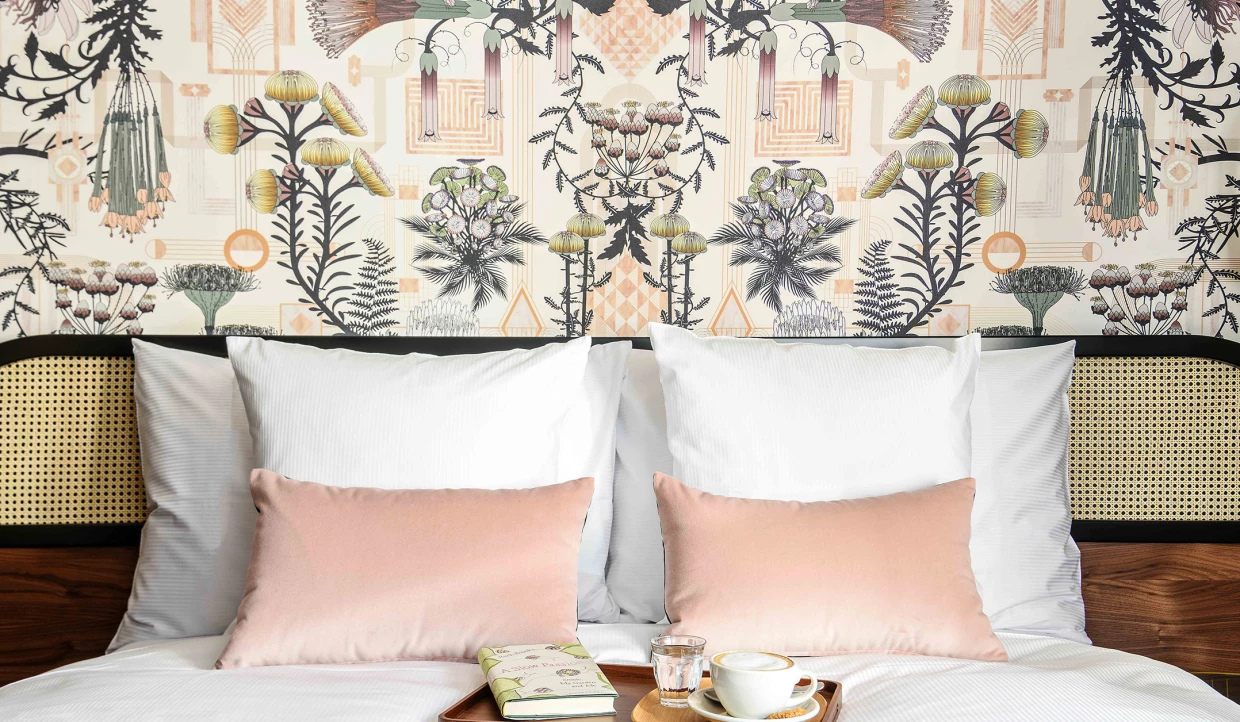 Kopfteil eines Doppelbetts in Hotelzimmer mit elegant-historischer Tapete mit botanischen Motiven und mehreren Kissen