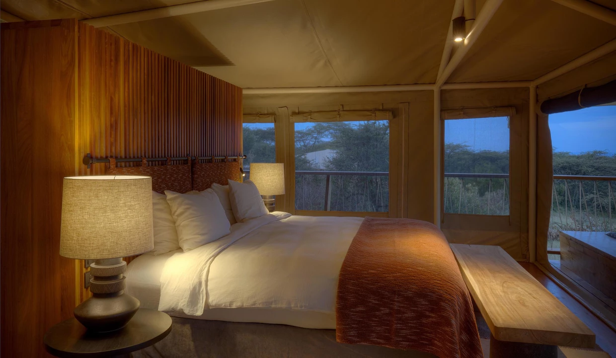 Gemütliches Bett in einem Luxus-Safari-Zelt mit grossen Lampen und Ausblick auf Savanne
