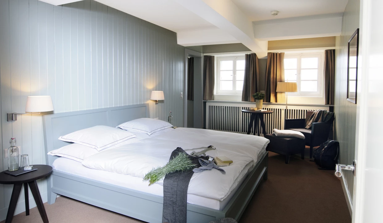 Helles Schlafzimmer mit Bett und Sessel neben Fenster.