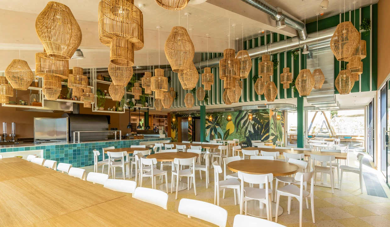 Restaurant mit runden Holztischen und weißen Stühlen, Hängelampen aus Rattan