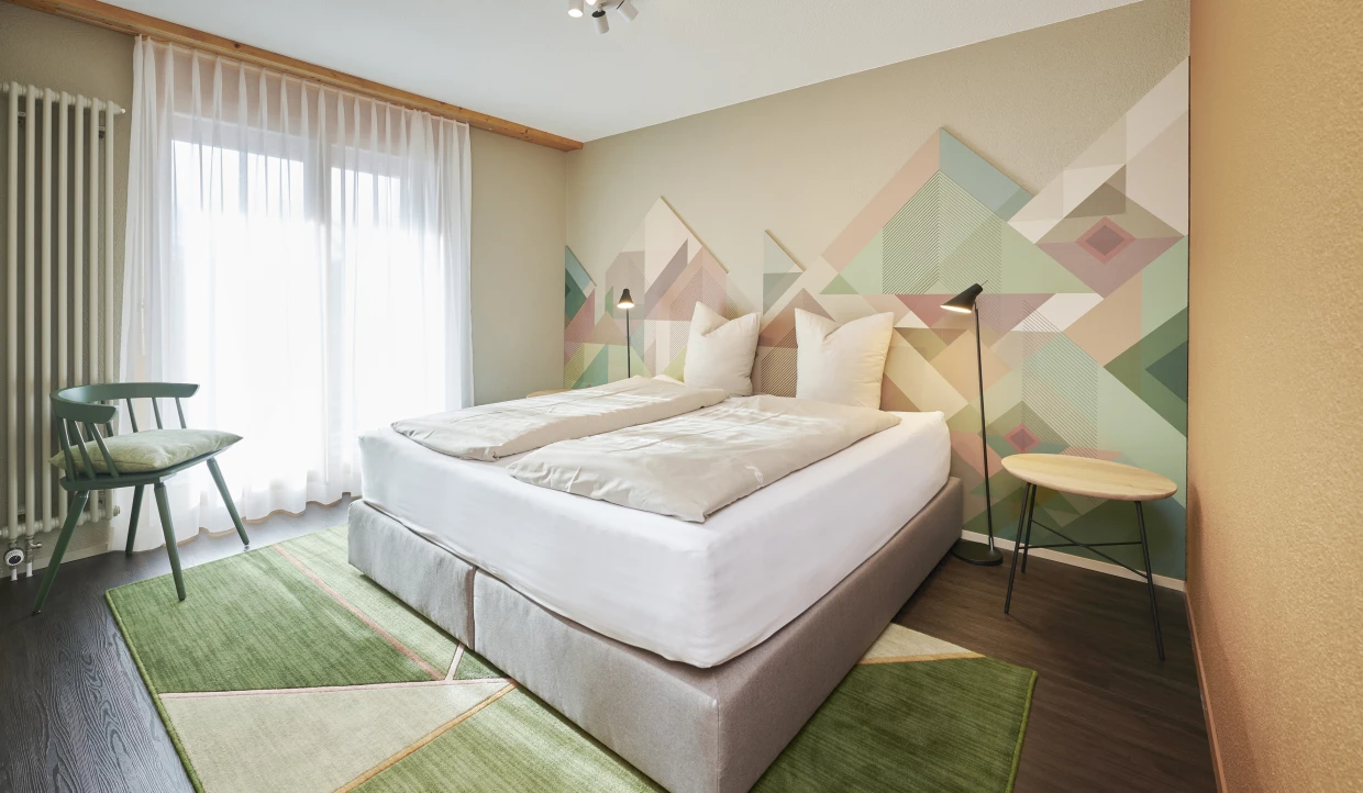 Schlafzimmer mit großem Fenster, Doppelbett und grünem Teppich