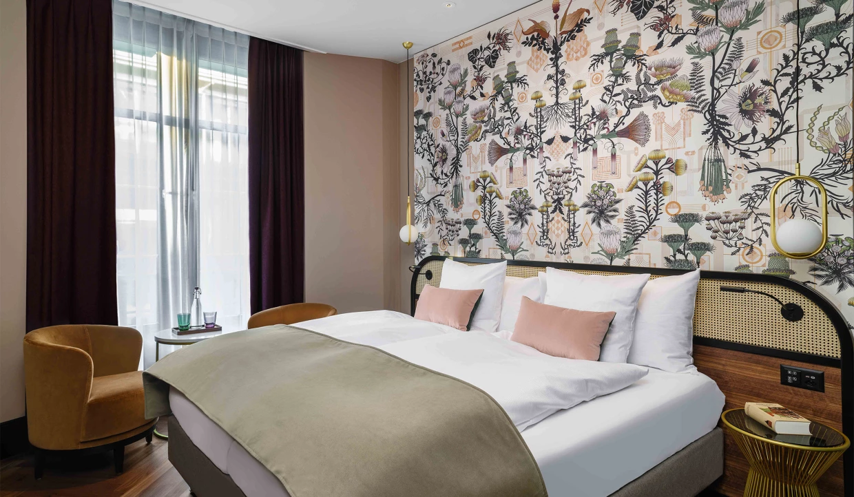 Hotelzimmer mit Doppelbett in Beige und Rosé, Wandtapete mit botanischen Motiven im Art-Deco- und Jugendstil-Mix.