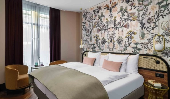 Hotelzimmer mit Doppelbett in Beige und Rosé, Wandtapete mit botanischen Motiven im Art-Deco- und Jugendstil-Mix.
