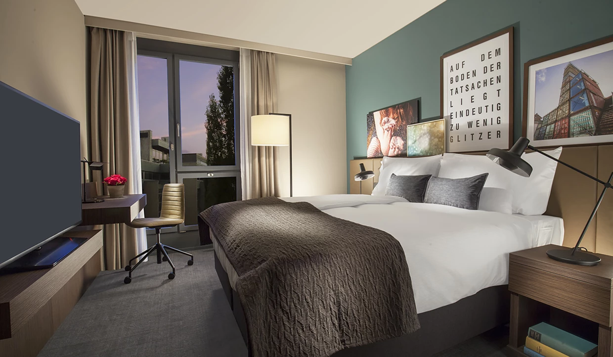 Zimmer mit Bett, Schreibtisch, Fenster und Kunstwerken