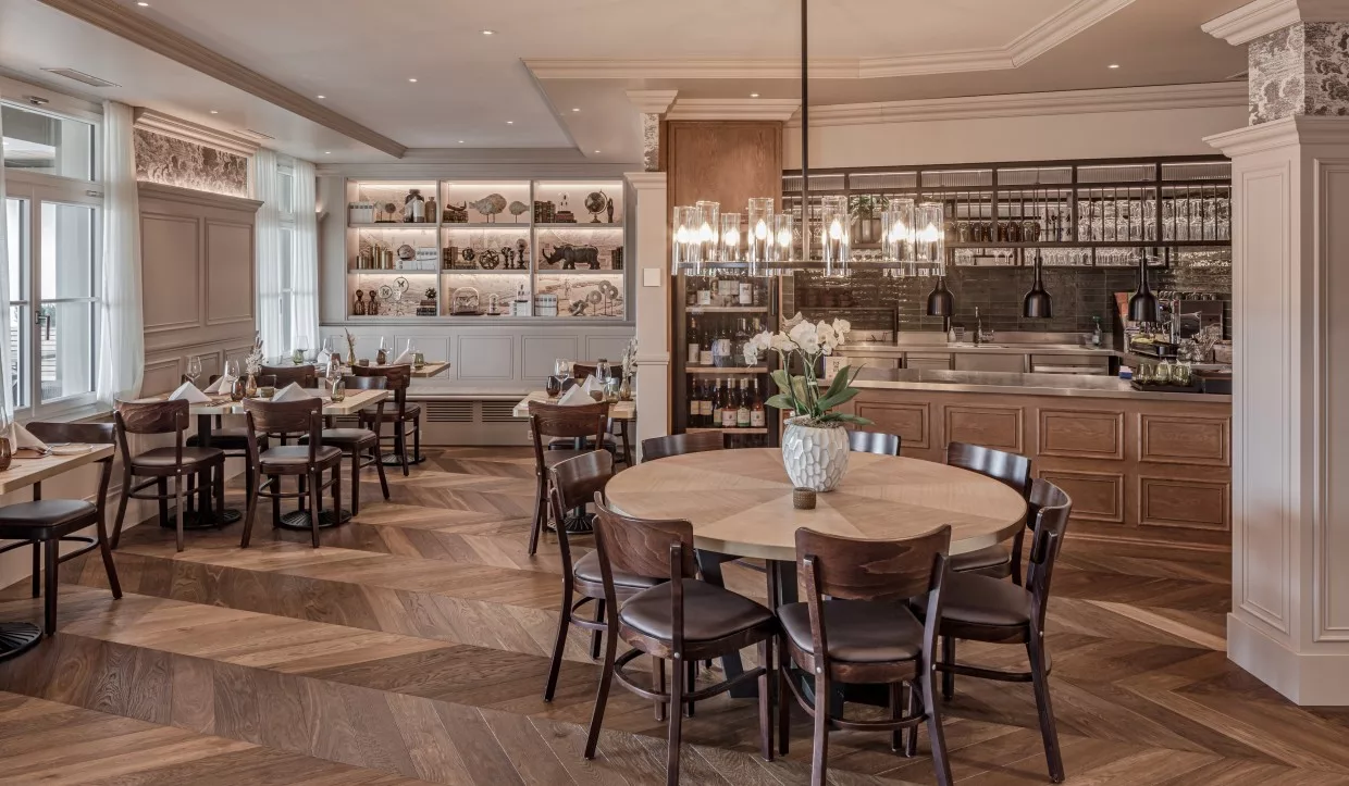 Modernes Landrestaurant in Holz mit runden Tischen und Küche im Hintergrund