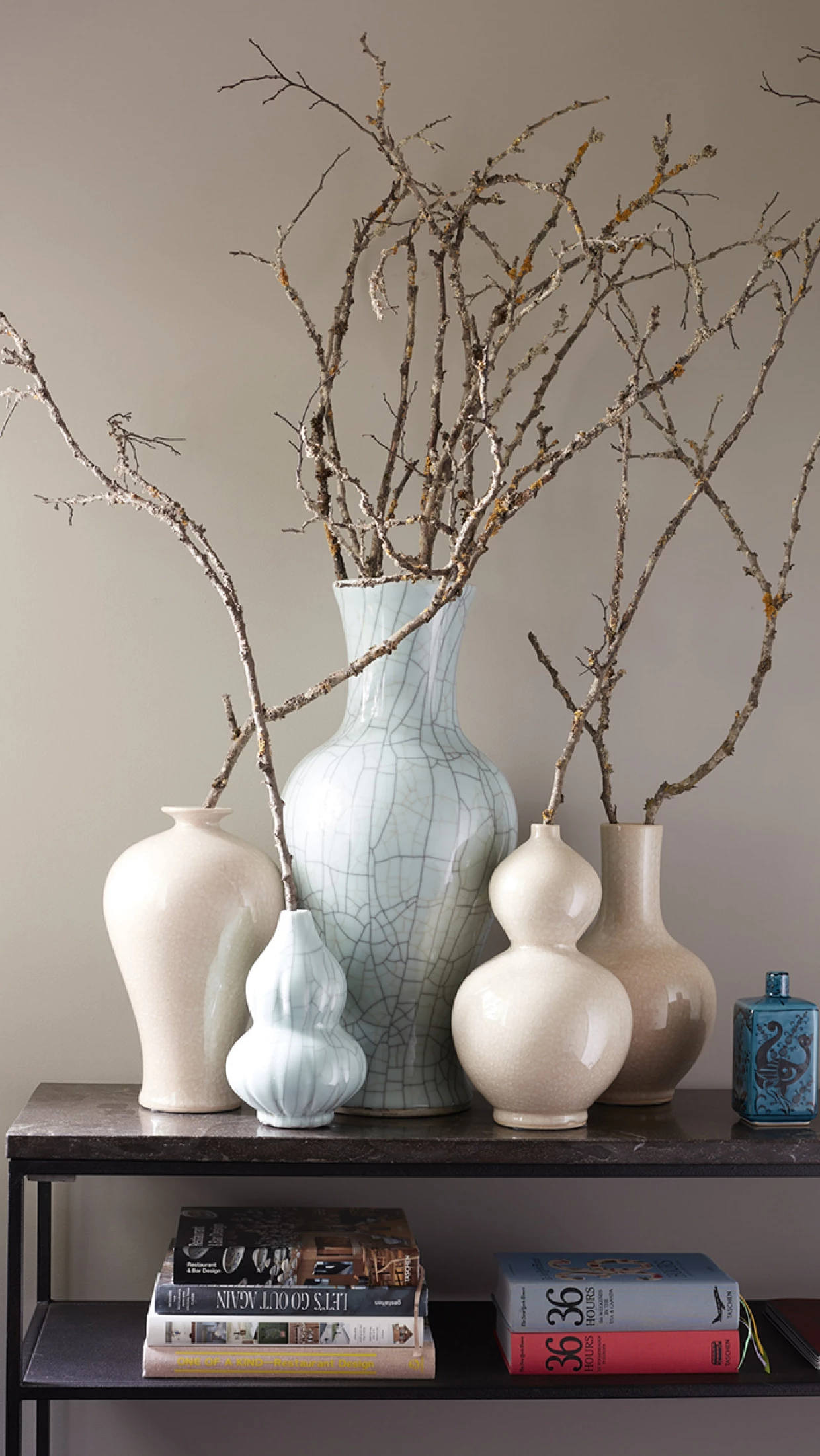 Decorative table with large vases and branches, books below