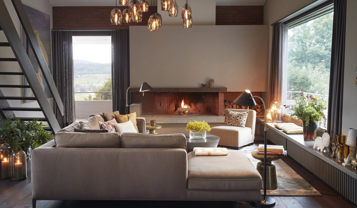 Living room with sofa, fireplace, pendulum lights, large windows