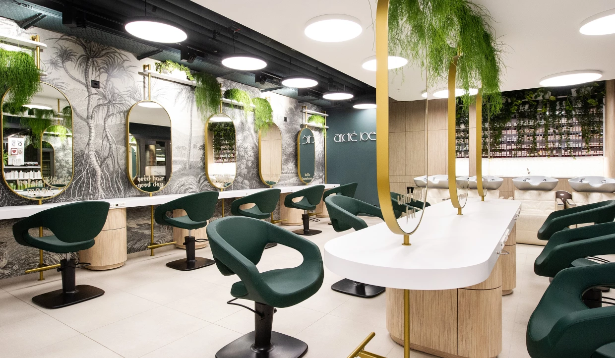 Geräumiger Salon mit grünen Stühlen, Spiegeln und Pflanzen