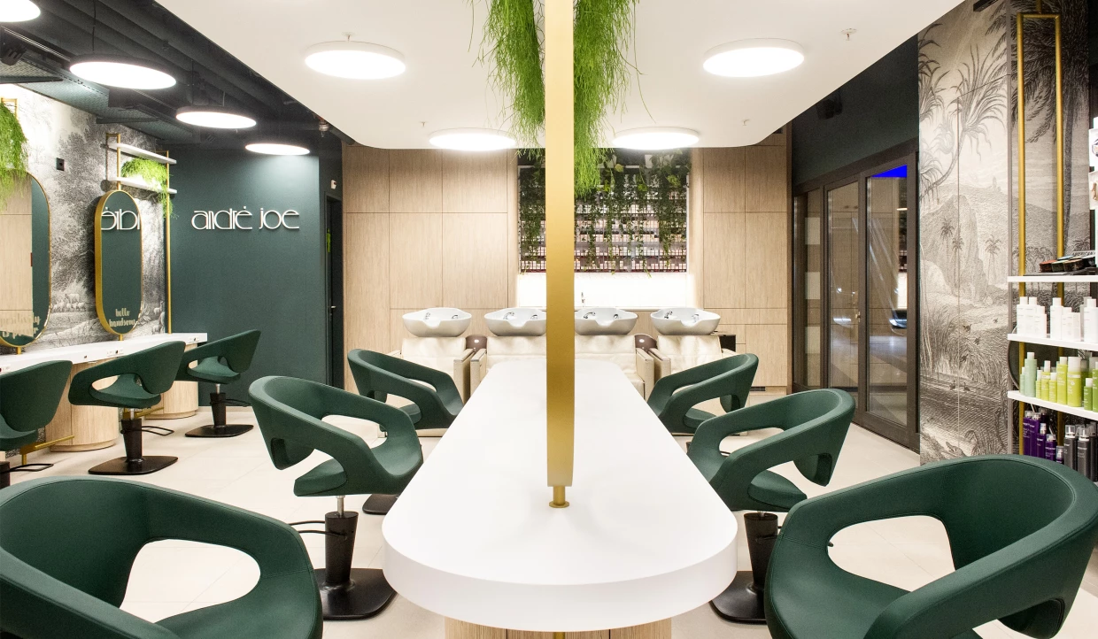 Zentraler Friseurtisch mit Spiegeln und grünen Salonstühlen umgeben