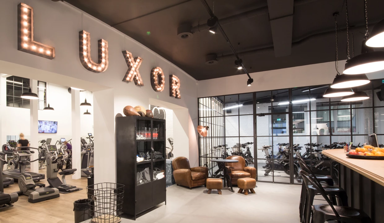 Fitnessstudio-Lobby mit Ledersesseln und Schriftzug 'LUXOR'
